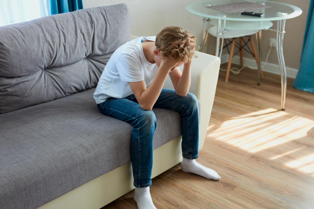 A boy sitting on the couch, with his hands on his head | Source: Shutterstock